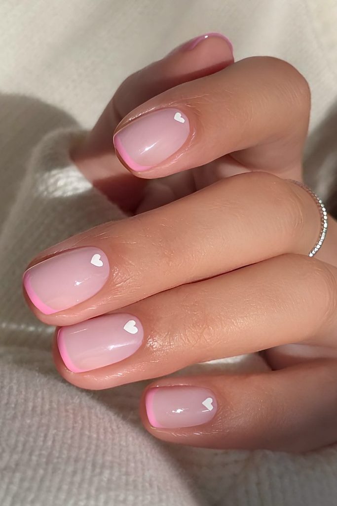 Short soft pink nails with white hearts and pink French tips, short milky pink nails with heart nail art, short light pink nails with a pink micro French, cute pink heart nails, Valentine’s Day nails, short square nails, simple nail art, minimalist nail design, glossy pink manicure